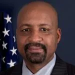 a man in a suit and tie standing in front of an american flag