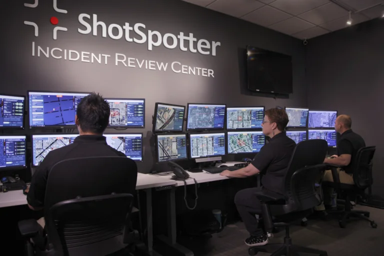 two men sitting in front of multiple computer monitors