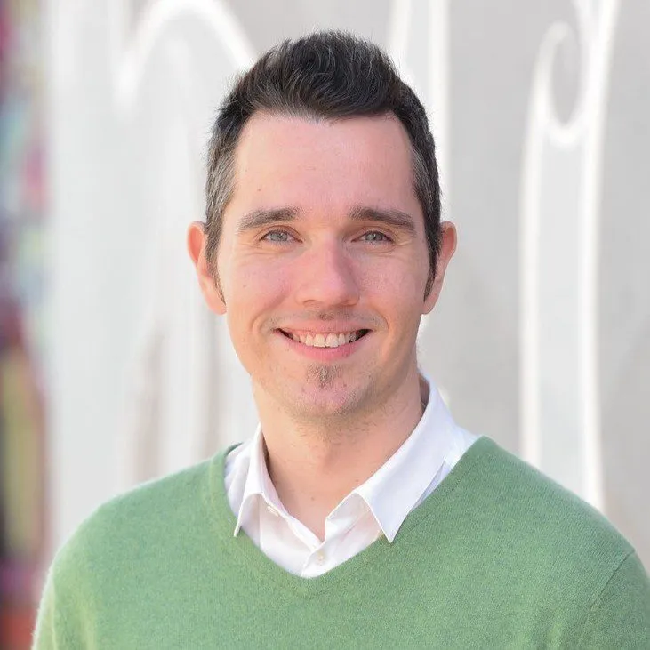 a man in a green sweater smiling at the camera