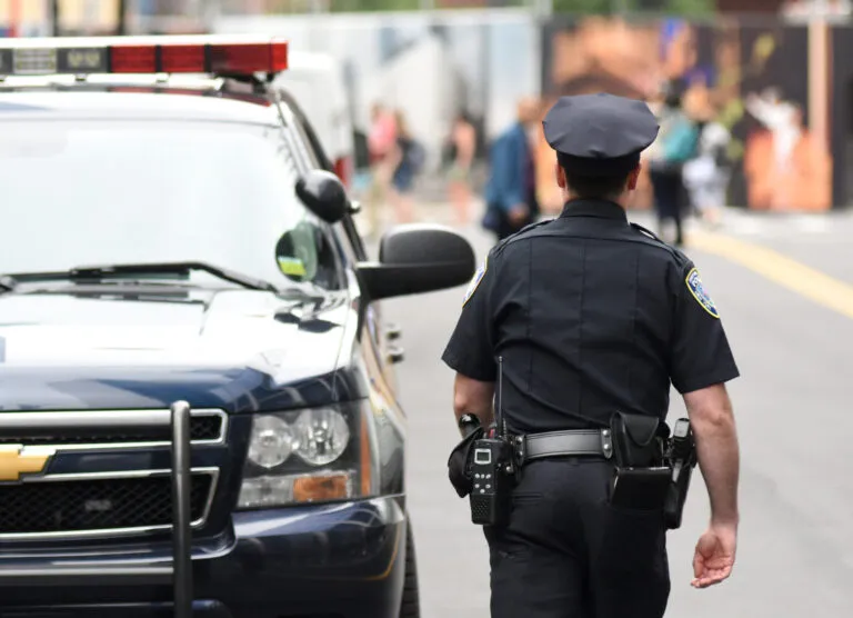 a police officer walking down a street next to a police car