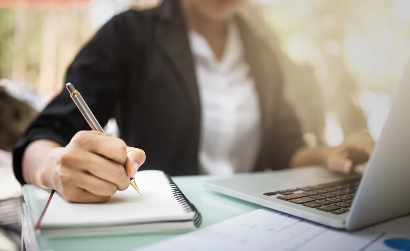 a woman sitting at a desk writing on a notebook