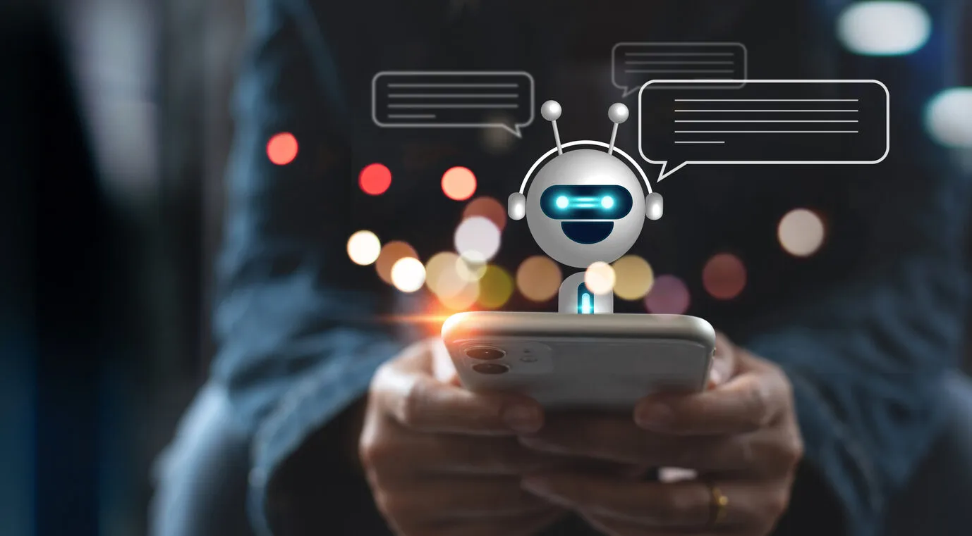 Stock image showing hands holding a mobile phone with a chatbot on top interacting.