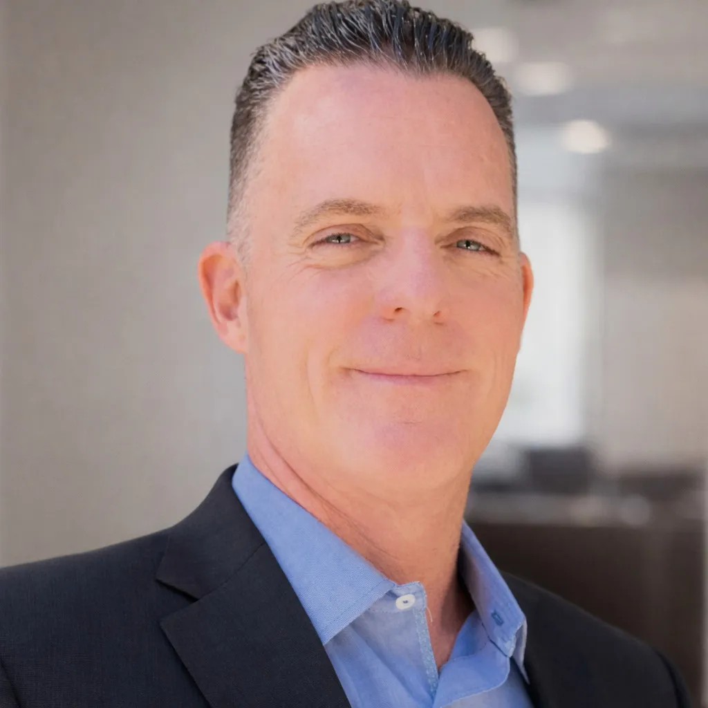 Headshot image of man in blue collared shirt under a blue suit jacket.